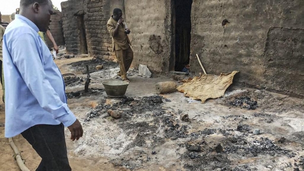 Des politiques et des habitants se tiennent près des cendres le 11 juin 2019 dans le village de Sobane, près de Sangha au Mali, après la tuerie du 9 juin 2019.