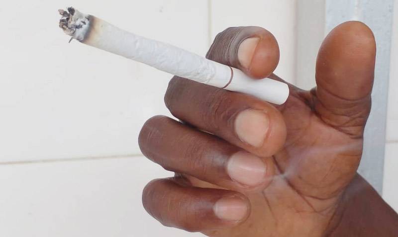 Un fumeur tenant entre ses doigts une tige de cigarette allumée. (Ph: Dr)