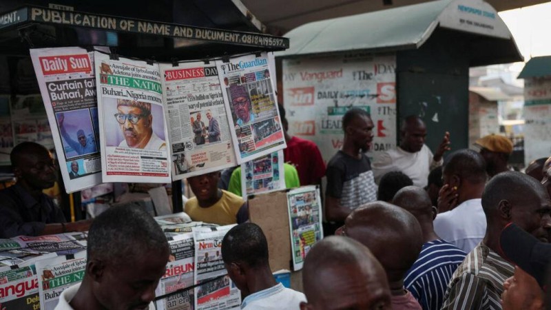  Des personnes lisent les titres des journaux annonçant la mort de l'ancien président nigérian Muhammadu Buhari dans un kiosque à journaux à Lagos, au Nigeria, le 14 juillet 2025. © Sodiq Adelakun / Reuters 
