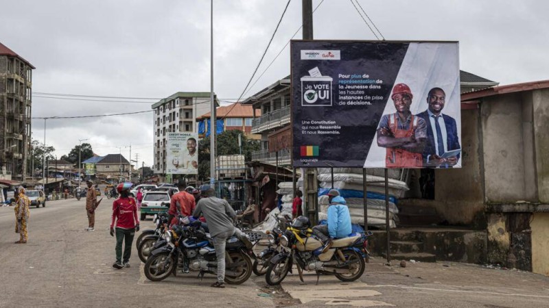  Des moto-taxis sont garées à côté d'un panneau d'affichage politique en faveur du « oui » au référendum constitutionnel à Conakry, le 3 septembre 2025, à l'approche du référendum constitutionnel du 21 septembre 2025. © Patrick Meinhardt / AFP 
